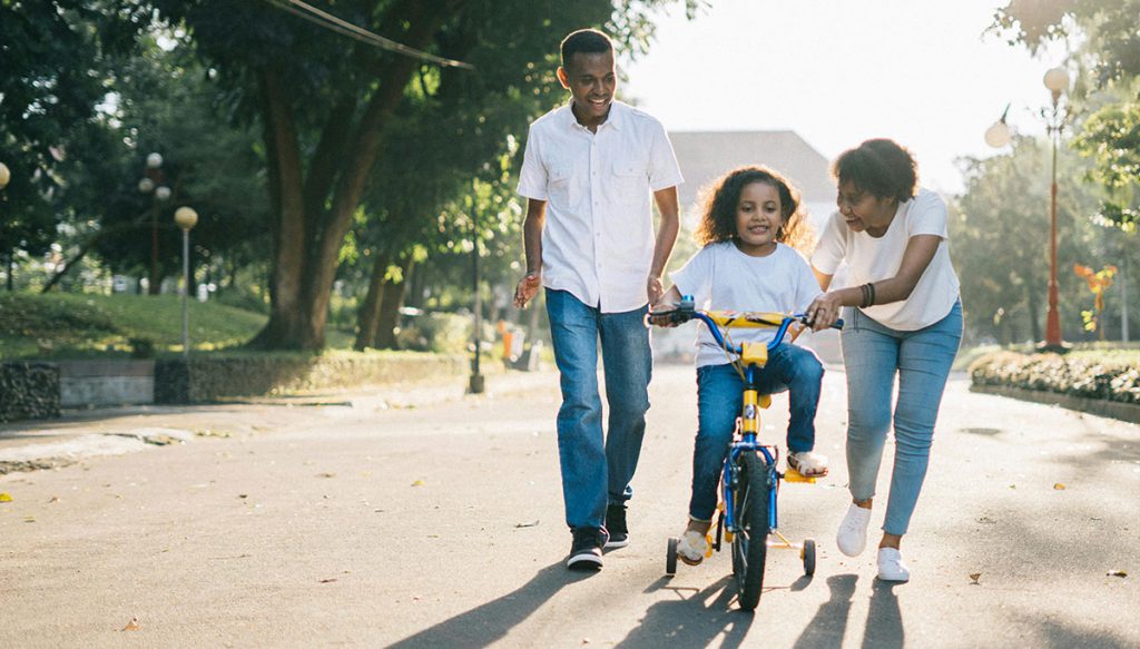 parents helping child ride a bicycle