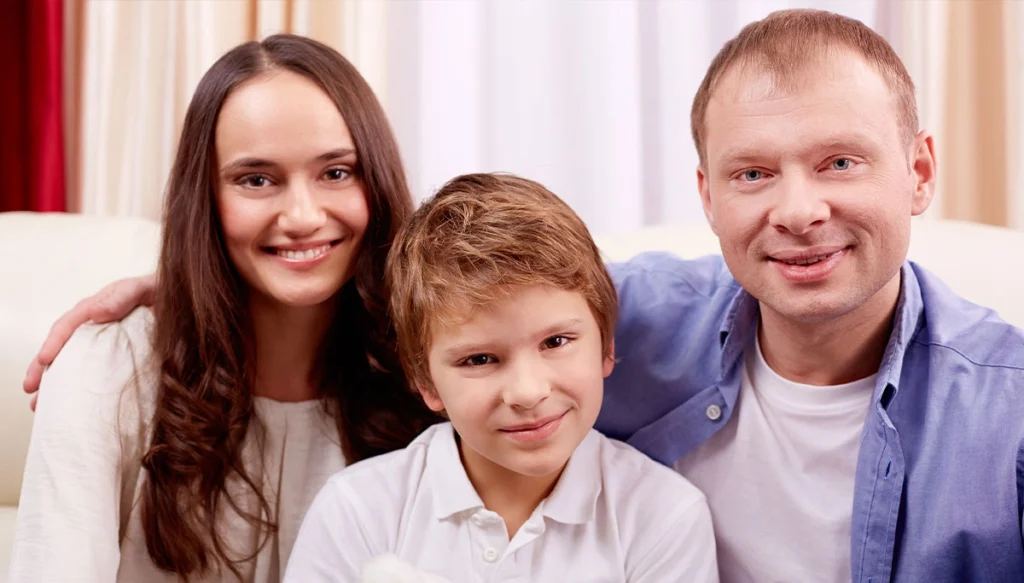 a mother father and young son smiling while sitting on a couch