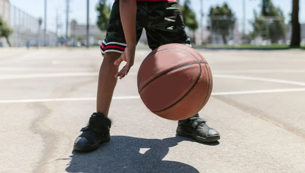 young child bouncing a basketball on a court on a bright summer day